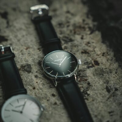 Stylish analog wristwatches with black leather straps displayed on a textured stone background.